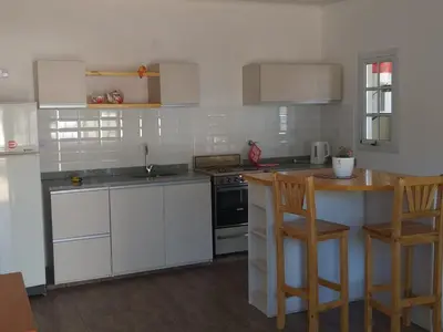a kitchen with white cabinets and a counter with chairs at Cabaña Los Pajaritos in Villa Rumipal