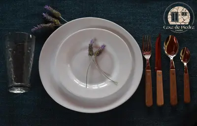 a white plate with a flower on it with forks and knives at Cabañas Casa de Piedra Los Molles - San Luis in Los Molles