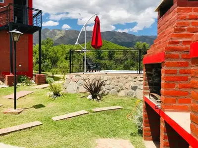 a yard with a brick building and a red umbrella at CABAÑA LA MILAGROS REINA MORA in Merlo