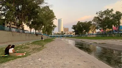 a couple of people sitting on the grass by a river at Encantador Duplex cerca de todo in Cordoba
