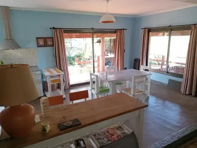 a living room with a table and chairs and windows at Casa Villa General Belgrano in Villa Ciudad Parque