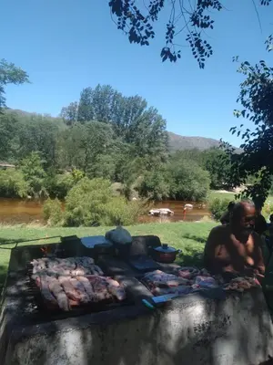 a man sitting next to a grill with food at Casa de montaña in Bialet Massé