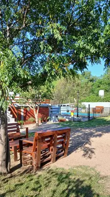 two wooden benches sitting under a tree in a park at El Molle in Estancia Vieja