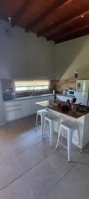 a kitchen with a table and two white stools at Casa en Potrero de Garay con pileta in Potrero de Garay