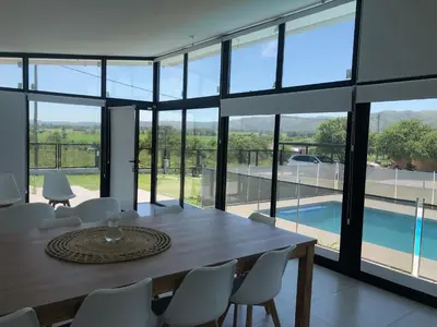 a dining room with a table and chairs and a pool at Olivos del Solar in Villa General Belgrano