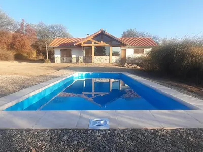 a blue swimming pool in front of a house at Atardecida in Villa de Las Rosas