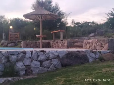 a stone wall with an umbrella next to a pool at Cabaña LA PEDRERA - Pileta y a metros del Rio in Bialet Massé
