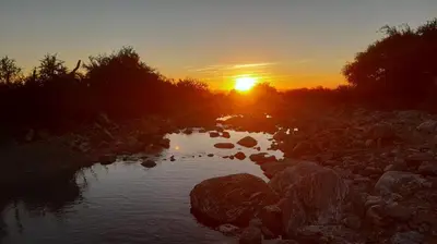 a sunset over a river with rocks and trees at Casa de montaña in Cortaderas
