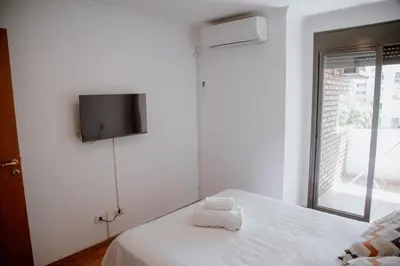 a bedroom with a white bed with a tv on the wall at Departamento en Obispo Trejo by Lofty in Cordoba