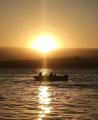 a boat in the water with the sun in the background at Cabañas Mirador de la Bahia in Villa Ciudad Parque