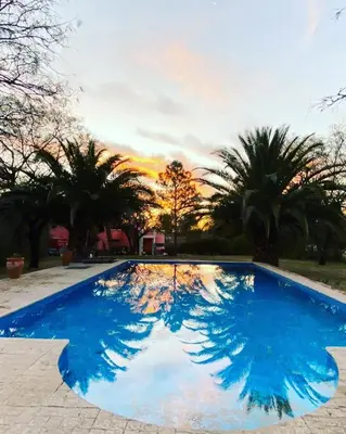 a blue swimming pool with palm trees and a sunset at La carolina in Villa de Las Rosas