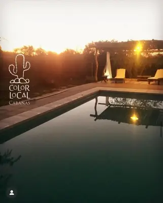 a swimming pool with two chairs and a sunset in the background at Color Local Cabañas in San Javier