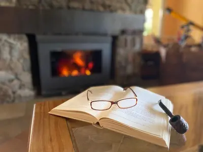 an open book with glasses and a pen on a table with a fireplace at Posada Sausalito in Santa Rosa de Calamuchita