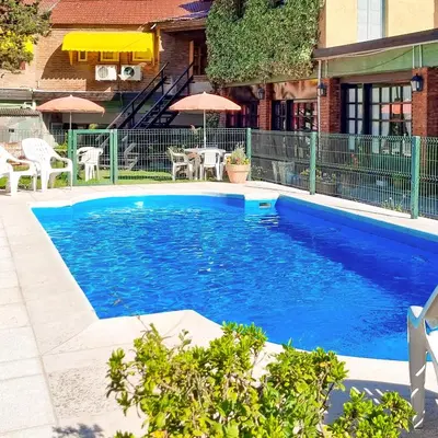 a large blue swimming pool with tables and umbrellas at POSADA NEHUEN in Villa General Belgrano